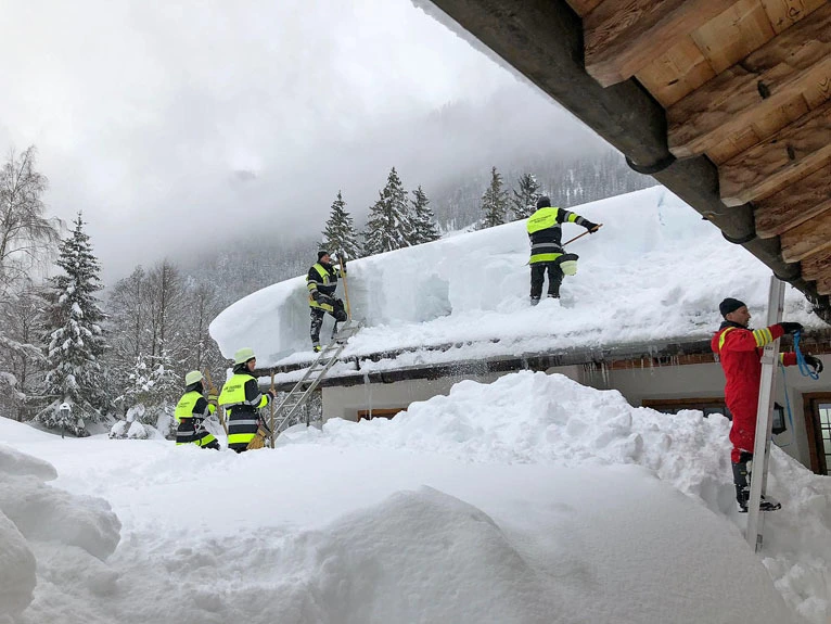 Einstazkräfte der Feuerwehr räumen den vielen Schnee von einem Hausdach — © Berufsfeuerwehr München
