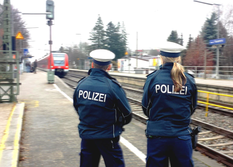 Zwei Bundespolizisten stehen an einem Bahnhof und warten auf die einfahrende S-Bahn — © Foto: Bundespolizei