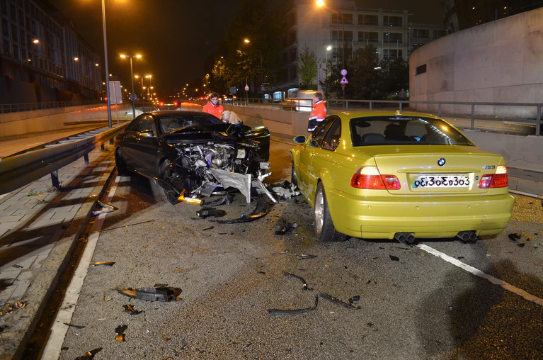 nahe Aufnahme der geschädigten Autos, Knautschzone des schwarzen Mercedes komplett demoliert, gelber BMW vorne links beschädigt, von hinten zu sehen, Autoteile auf der Straße verteilt. — © Foto: Polizei