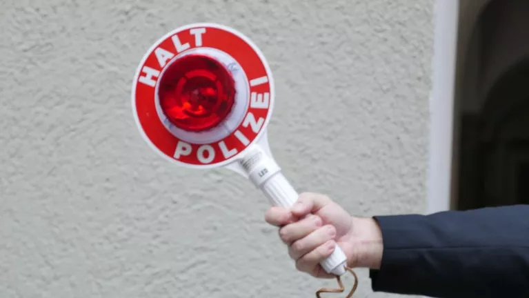Halt Polizei schild rot weiß in hand gehalten vor grauer wand