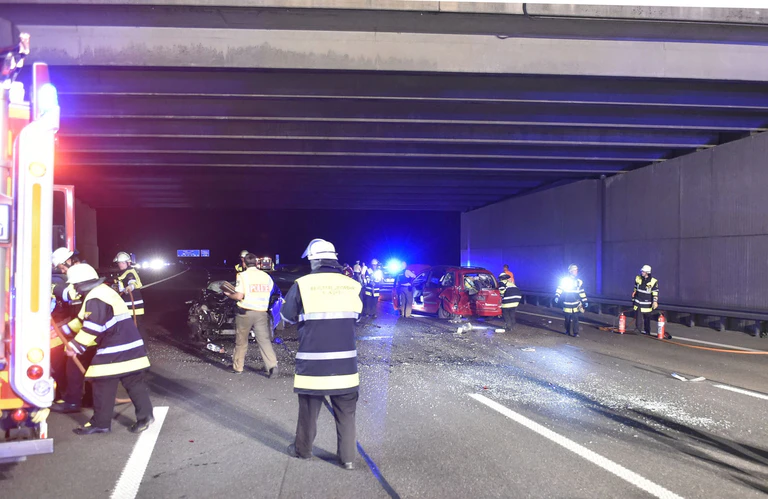 Unfallstelle mit Feuerwehreinsatzkräften und roten Unfallauto unter Straßentunnel — © Feuerwehr München