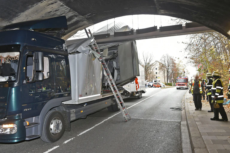 Ein kaputter LKW steckt in einer Unterführung fest, daneben stehen Feuerwehrleute — © Berufsfeuerwehr München